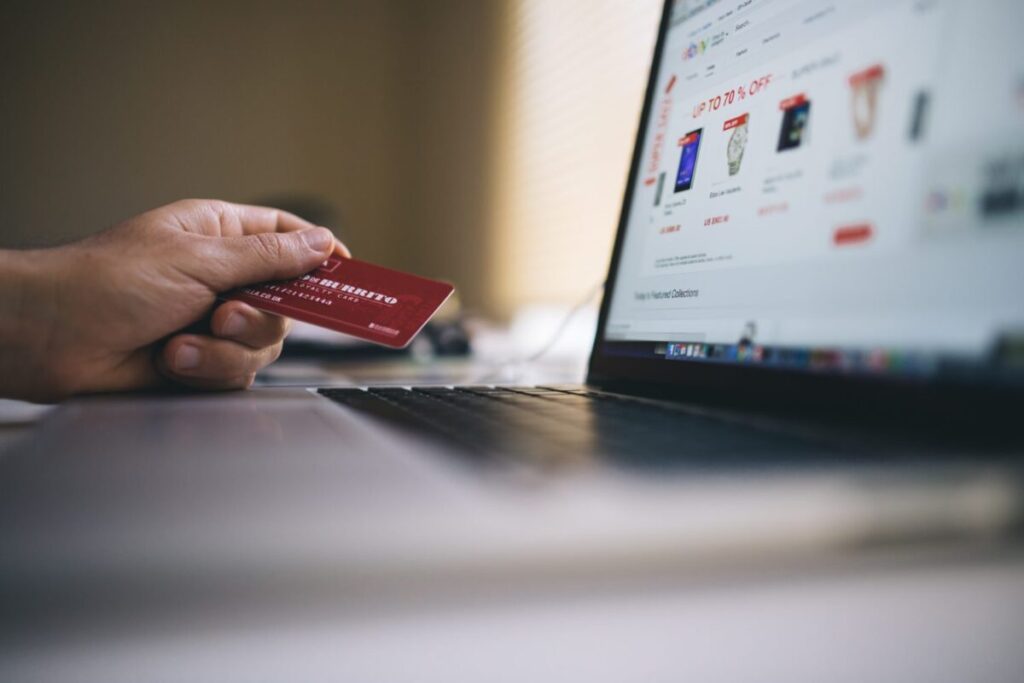 Hand of a person facing holiday debt, holding credit card and looking at their balance on a computer screen